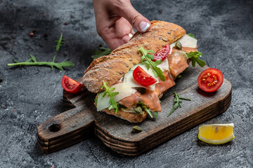 Woman hands holds Sandwiches with homemade ciabatta bread, salted salmon fish, parmesan cheese,...