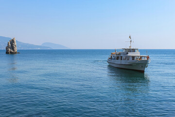 Fototapeta na wymiar Excursion steamer on a smooth sea surface. The background is a blue sky and mountains. Beautiful seascape. Excursion tourism. Yalta, Crimea.