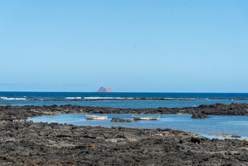 Vista panorámica de la costa de Lanzarote con barcos navegando por sus aguas cristalinas y La Graciosa al fondo durante un día soleado con el cielo azul. Recursos naturales de Islas Canarias