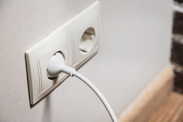 Close-up of a white electric plug in a 220 socket in the wall. Power on concept