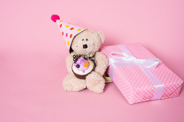 Cute teddy bear with gift box on pink background. Birthday celebration concept.