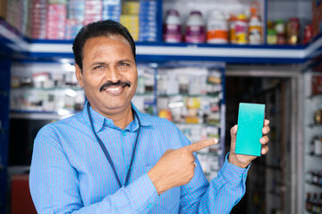 smiling medical shop owner showing green screen mobile phone by looking at camera - concept of...