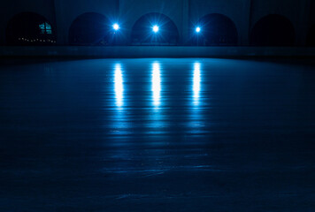 Smooth, shiny surface of an ice rink with reflected by spotlights. Dark empty ice arena with soft blue light. Concept of winter sports games, hockey, figure skating. Icy background of slippery ice.