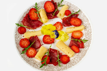 Salad with strawberry, cheese and carpaccio, edible pansy flower and rucola leaf on plate, isolated on white.