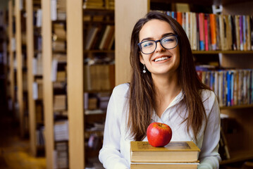 Happy female student with pile of books in the library. Smiling attractive girl eager to study and get new knowledge