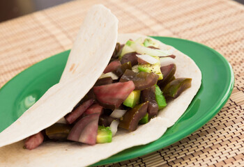 salad of black tomatoes, avocado and onions in Italian tortilla on green plate