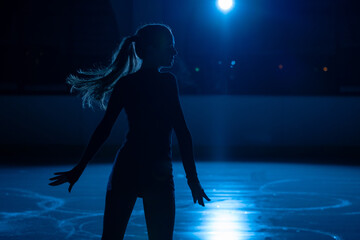 Young female figure skater is performing woman's single skating choreography on ice rink....