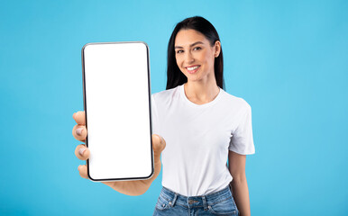 Happy young lady demonstrating big cellphone with white screen, showing space for your design, mockup