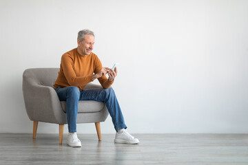 Portrait of mature man using smartphone sitting on armchair
