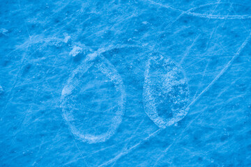 Ice surface in sports arena for figure skating or hockey. Ice background and ice texture is cut with pattern and scratches from skates. Detail of textured ice with snow in blue light. Close up.