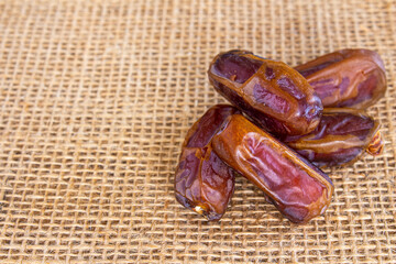 Stack of date fruits on burlap background, space for text
