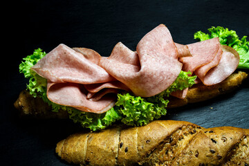 complete deli sandwich kornspitz whole grain filled with meat slices and salad over dark background with copy space