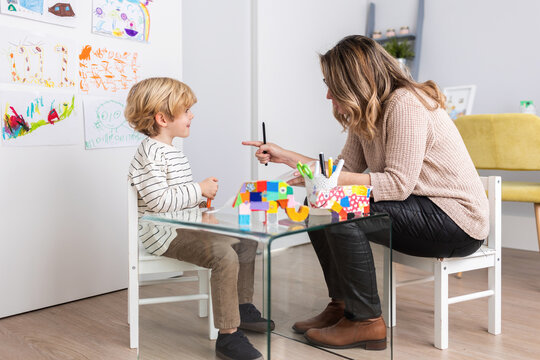Psychologist sitting near boy drawing on paper