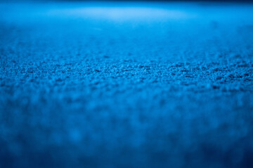Low angle on ice surface in arena for figure skating or hockey. Ice background and ice texture is cut with pattern and scratches from skates. Detail of textured ice with snow in blue light. Close up.