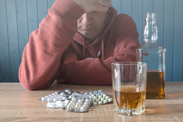 Stress. Blisters with antidepressants, pills, alcohol lie on the table. Addiction. Emotional burnout. Alcohol addiction. Blurred silhouette of a man.