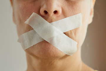 Close-up of a woman's mouth is sealed with a white tape with a cross. Diet concept. Deprivation of freedom of speech.
