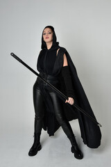 Full length portrait of pretty redhead female model wearing black futuristic scifi leather costume,...