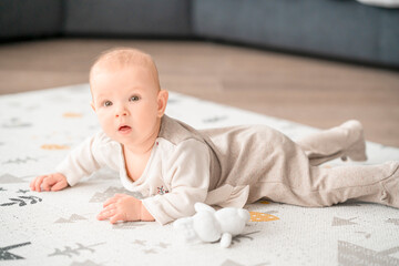 Baby lies on his stomach and looking at camera on the play mat. Happy childhood