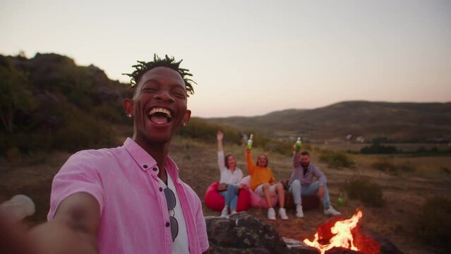 African american man takes selfie with his friends at camping, they laughing and smiling, hold alcoholic cocktails and drinks their hands. Black man takes pictures of himself friends in outdoor