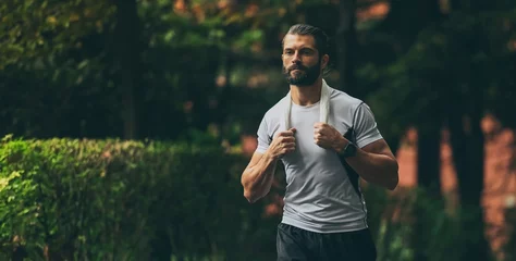 Foto op Canvas Determined young man running outside in the park. Fit boy doing exercise outdoor. Beautiful sporty male run alone. Sweaty athlete training with towel. Wellness, health, sport, fitness open air concept © Fabio Principe