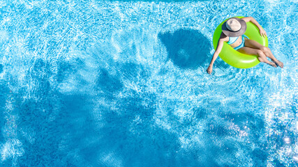 Active young girl in swimming pool aerial top view from above, teenager relaxes and swims on inflatable ring donut and has fun in water on family vacation, tropical holiday resort
