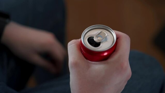 A man's hand opens a can of carbonated drink, possibly Coca-Cola