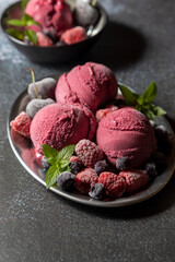 Homemade blueberry ice cream scoops with fresh berries and mint leaves in cups over light blue background, selective focus