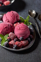 Homemade blueberry ice cream scoops with fresh berries and mint leaves in cups over light blue background, selective focus