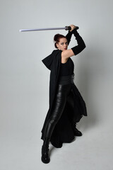 Full length portrait of pretty redhead female model wearing black futuristic scifi leather cloak...