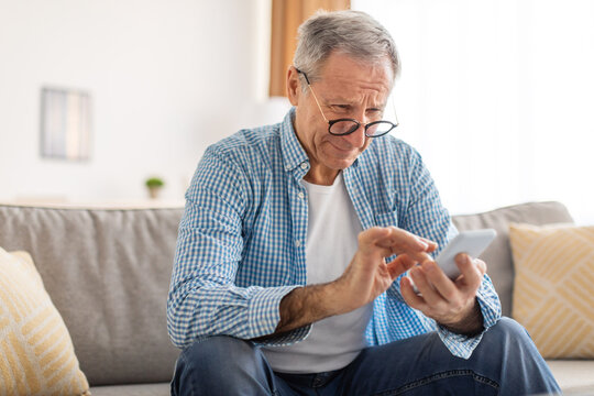 Mature man squinting using cell phone, looking at screen