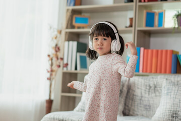 Happy Asian child having fun listening to the music with the headphones and dancing in a room