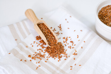 Flax seeds in a round plate with wooden spoon on a linen napkin in a kitchen. Ingredient for flaxseed porridge and jelly. Minimalistic simple natural light template. Superfood. Organic eco healthcare.