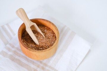 Fototapeta na wymiar Flax seeds in a round plate with wooden spoon on a linen napkin in a kitchen. Ingredient for flaxseed porridge and jelly. Minimalistic simple natural light template. Superfood. Organic eco healthcare.