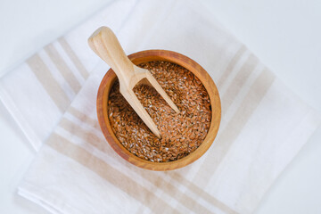 Flax seeds in a round plate with wooden spoon on a linen napkin in a kitchen. Ingredient for flaxseed porridge and jelly. Minimalistic simple natural light template. Superfood. Organic eco healthcare.
