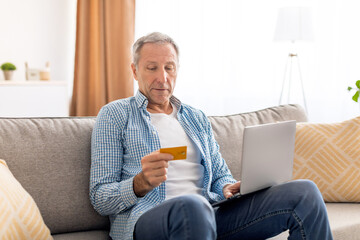 Focused mature man using pc and credit card at home