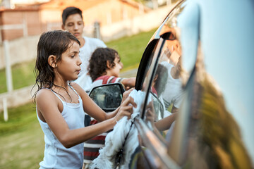 Some scrubbing here and some scrubbing there. Shot of a group of cheerful young kids washing their parents car together outside during the day. - Powered by Adobe