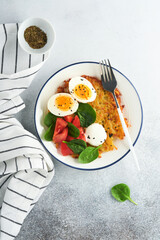 Breakfast. Potatoes latkes with sour cream, spinach salad, tomatoes and boiled eggs on light background.  Delicious food for breakfast. Top view.