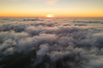Fototapeta na wymiar Aerial view from above at high altitude of dense puffy cumulus clouds flying in evening. Amazing sunset from airplane window point of view