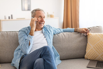 Cheerful mature man talking on cellphone sitting on couch