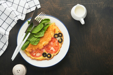 Omelette with tomatoes, black olives, cottage cheese and green spinach herbs on white plate on old wooden rustic dark background. Delicious breakfast. Healthy breakfast food. Top view.