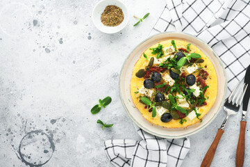 Scrambled eggs. Light, Fluffy and Buttery Scrambled Eggs with feta cheese, sun-dried tomatoes and black olives on plate over white stone background. Delicious breakfast. Top view, flat lay.