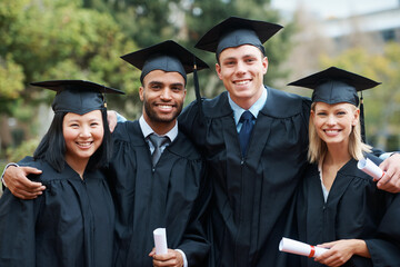 Students and fellow graduates. A group of college graduates standing in cap and gown and holding...