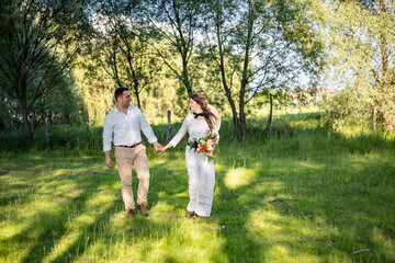 Naklejka na ściany i meble Happy young people in wedding attire walk in the meadow and look at each other