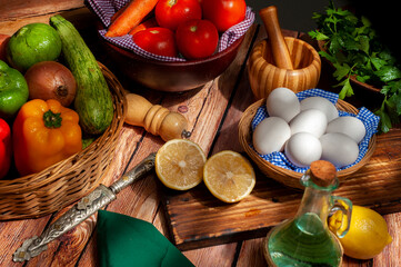 still life of vegetables, bell peppers onion, tomatoes, carrots and parsley with old oil can pepper shaker basket with white eggs on wooden table