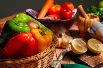 still life of vegetables, bell peppers onion, tomatoes, carrots and parsley with old oil can pepper shaker basket with white eggs on wooden table