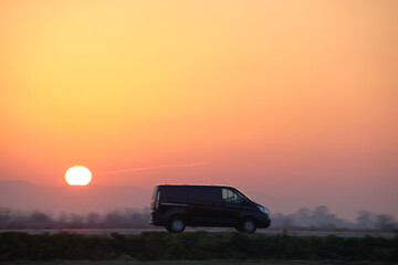 Fototapeta na wymiar Passenger van driving fast on intercity road at sunset. Highway traffic in evening