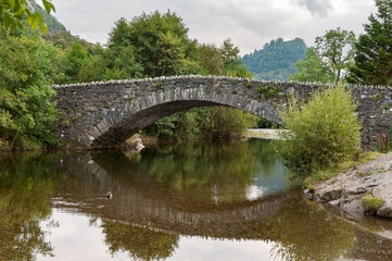 Fototapeta na wymiar The arched packhorse bridge across the river Derwent in Grange in Borrowdale in the English Lake District with Castle Crag in the background.