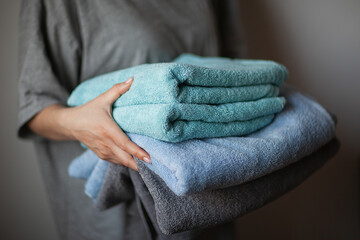 home laundry, female hand holding stack of clean bath towels colorful cotton terry textile background close up, selective focus