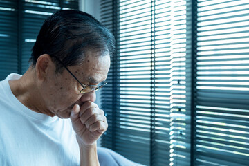 senior asian man coughing wearing glasses, after waking up in the morning, in the bedroom, wearing...