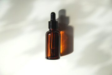 A brown glass dropper bottle on a white background casts a shadow with natural light. Top view copy space. Cosmetic product mockup. Serum for skin care.